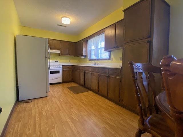 kitchen featuring visible vents, under cabinet range hood, light wood-type flooring, light countertops, and white appliances