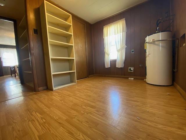 unfurnished living room featuring water heater, wood walls, light wood-type flooring, and baseboards