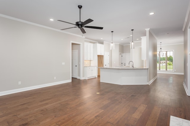 unfurnished living room featuring sink, dark wood-type flooring, ceiling fan with notable chandelier, and ornamental molding