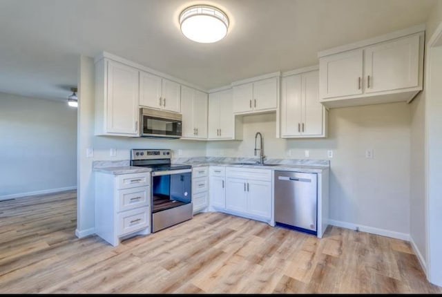 kitchen with appliances with stainless steel finishes, light stone counters, sink, light hardwood / wood-style floors, and white cabinetry