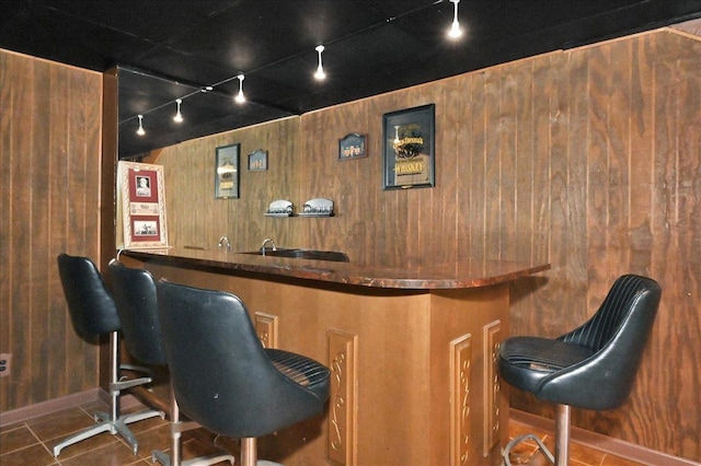 bar with wood walls, dark tile patterned floors, and track lighting