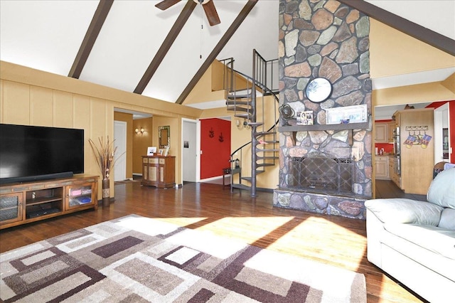 living room featuring dark hardwood / wood-style flooring, ceiling fan, beam ceiling, high vaulted ceiling, and a stone fireplace