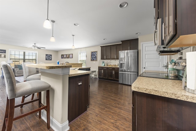 kitchen featuring a kitchen bar, dark brown cabinets, a kitchen island with sink, decorative light fixtures, and stainless steel fridge with ice dispenser