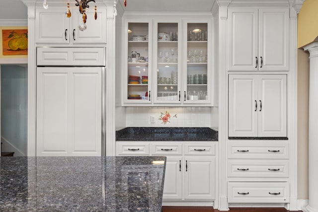 bar featuring tasteful backsplash, ornamental molding, dark stone counters, paneled built in fridge, and white cabinetry