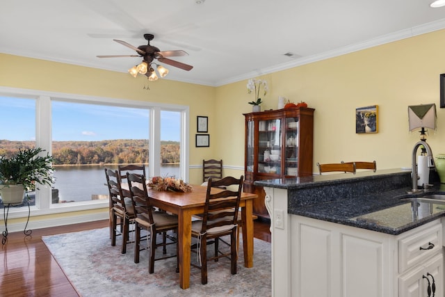 dining space featuring ceiling fan, sink, wood-type flooring, a water view, and ornamental molding