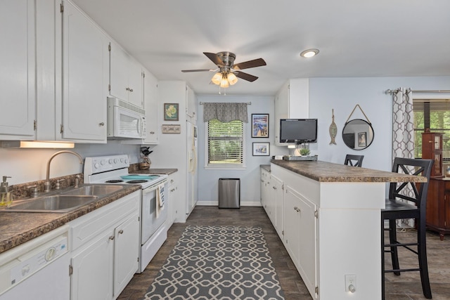 kitchen with white appliances, a sink, a peninsula, a ceiling fan, and a breakfast bar area