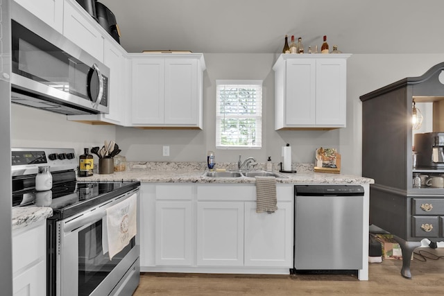  - kitchen featuring appliances with stainless steel finishes, a sink, light wood-style flooring, white cabinetry, and light stone counters
