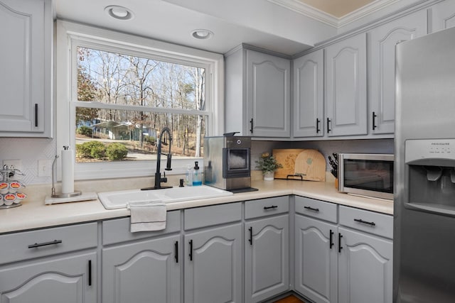 kitchen with gray cabinetry, a sink, appliances with stainless steel finishes, tasteful backsplash, and crown molding