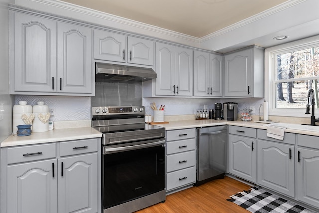 kitchen with stainless steel appliances, gray cabinets, light wood-style floors, a sink, and under cabinet range hood