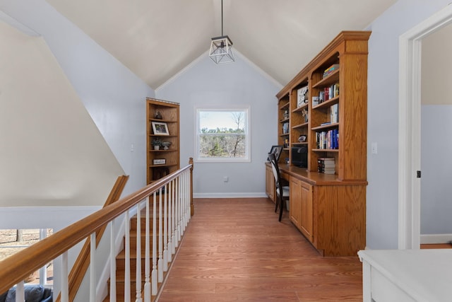 hall with an upstairs landing, light wood-type flooring, vaulted ceiling, and baseboards