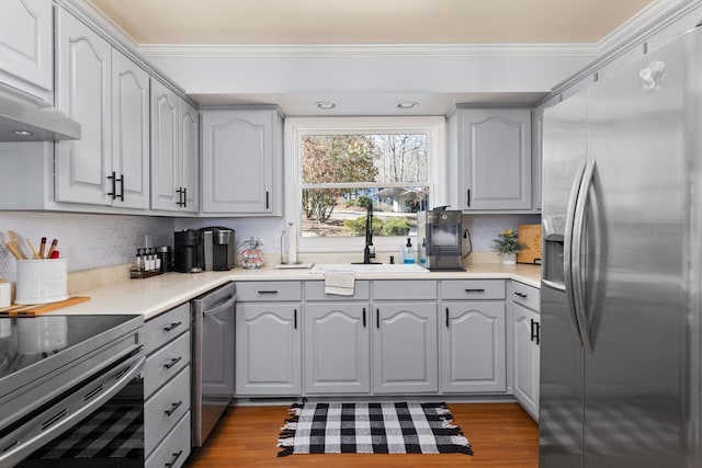 kitchen with gray cabinets, stainless steel appliances, crown molding, and wood finished floors