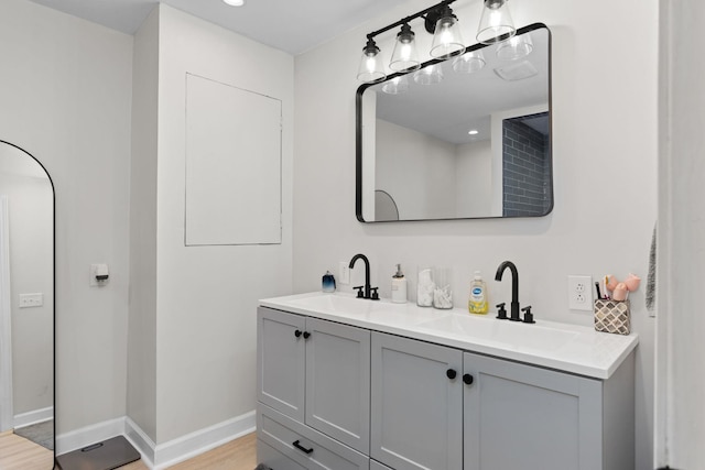 bathroom with wood finished floors, a sink, baseboards, and double vanity