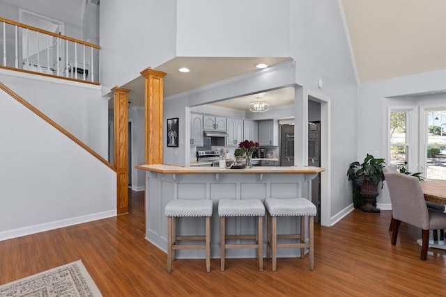 kitchen with a breakfast bar, decorative columns, wood finished floors, high vaulted ceiling, and baseboards