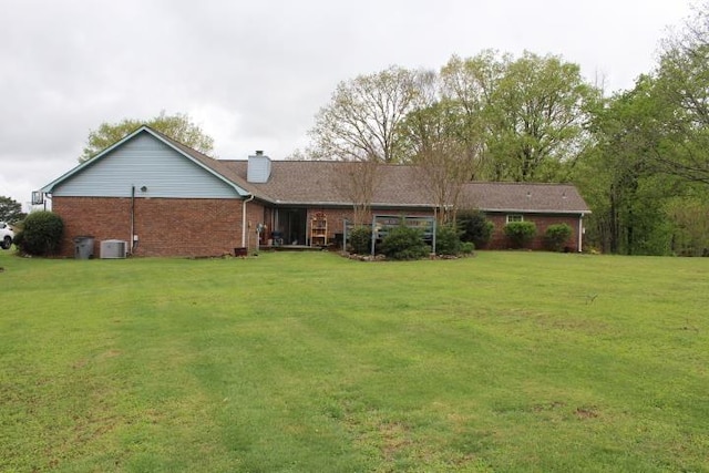 back of property with cooling unit, a chimney, brick siding, and a lawn