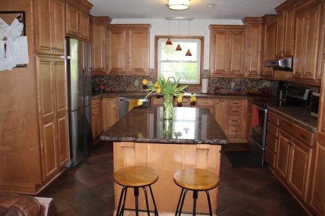 kitchen with under cabinet range hood, brown cabinets, a breakfast bar area, decorative backsplash, and stainless steel appliances