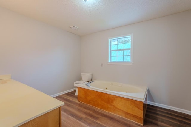 bathroom with a washtub, wood-type flooring, a textured ceiling, toilet, and vanity