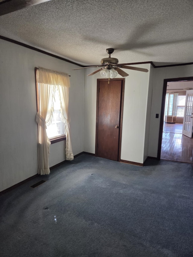 empty room with ornamental molding, dark colored carpet, visible vents, and a textured ceiling