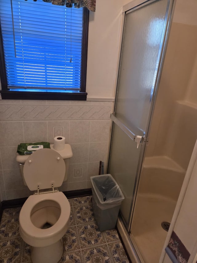 full bathroom featuring tile patterned flooring, toilet, a wainscoted wall, tile walls, and a shower stall