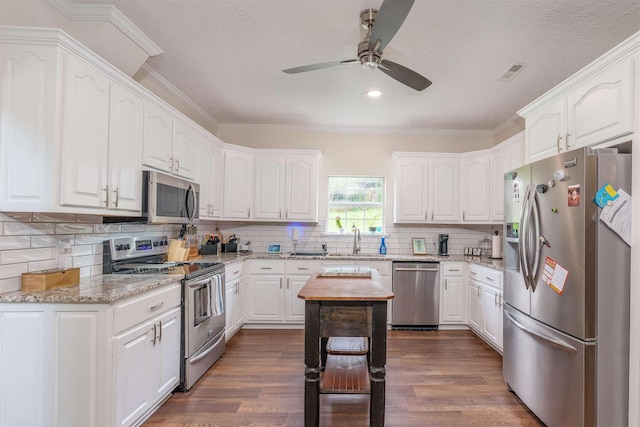  - kitchen with stainless steel appliances, ceiling fan, white cabinets, dark wood-type flooring, and ornamental molding