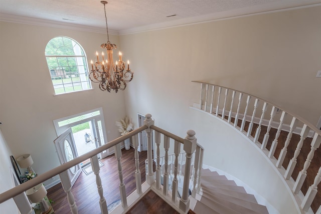  - staircase with wood finished floors, ornamental molding, a chandelier, a high ceiling, and a textured ceiling