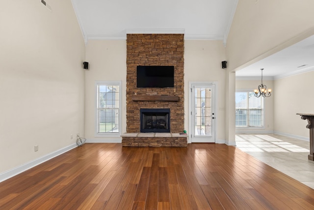 unfurnished living room featuring crown molding, hardwood / wood-style flooring, a chandelier, a high ceiling, and a stone fireplace