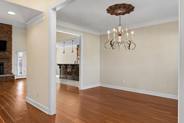 unfurnished dining area featuring hardwood / wood-style flooring, a stone fireplace, ornamental molding, and a chandelier