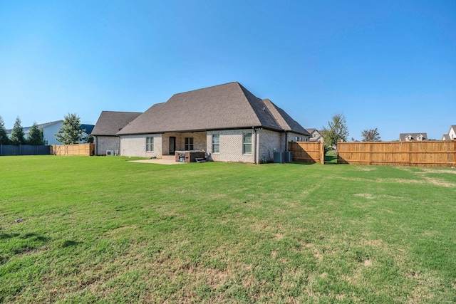 rear view of property with a fenced backyard, a yard, a patio area, central AC, and brick siding