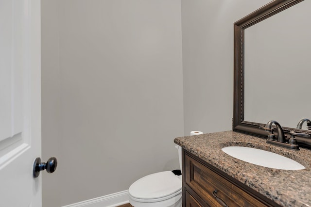 half bathroom featuring toilet, vanity, and baseboards