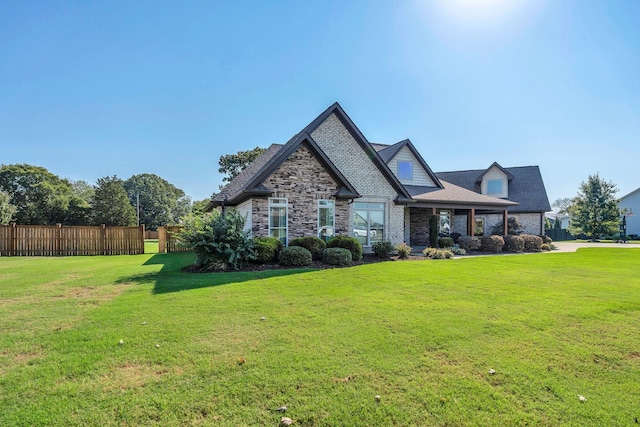 view of front of home with a front yard, stone siding, and fence