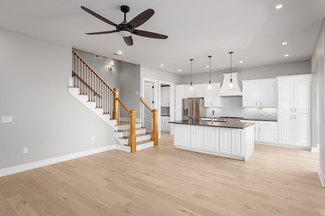 kitchen with premium range hood, a sink, light wood finished floors, dark countertops, and stainless steel fridge