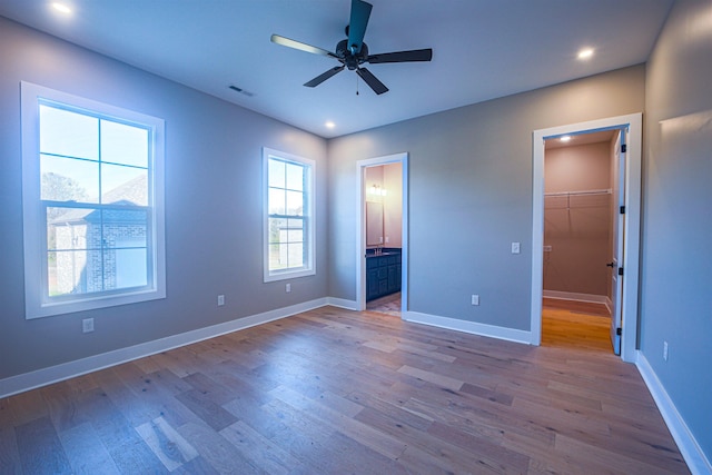 unfurnished bedroom featuring ensuite bathroom, ceiling fan, a spacious closet, light hardwood / wood-style floors, and a closet