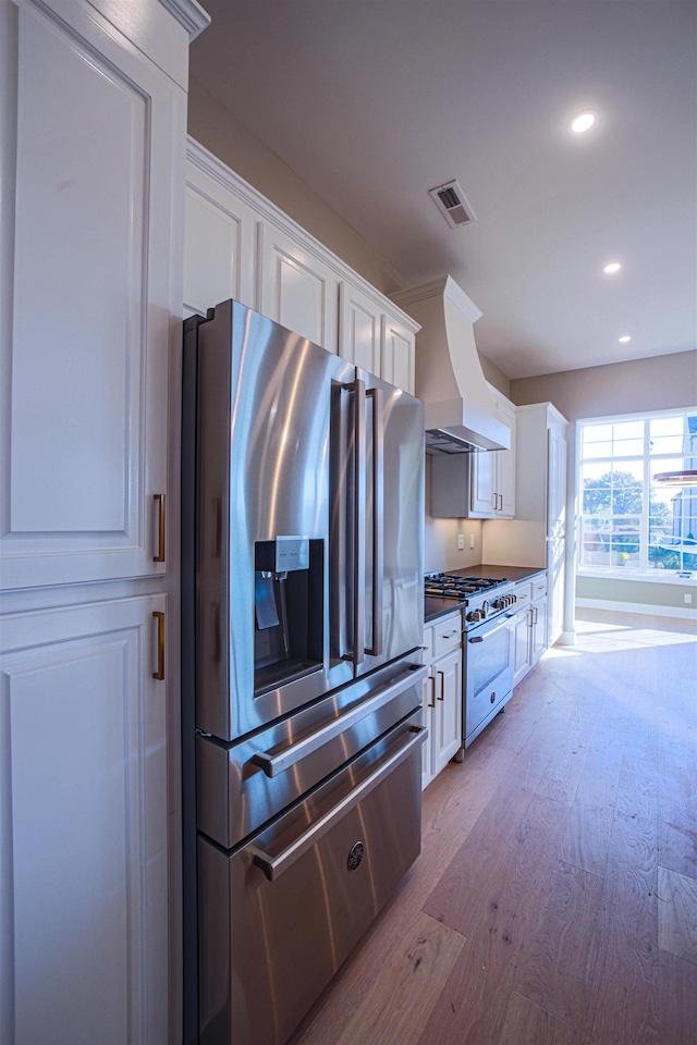 kitchen featuring appliances with stainless steel finishes, light hardwood / wood-style flooring, white cabinetry, and wall chimney range hood