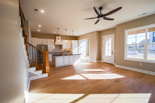 kitchen with ceiling fan, pendant lighting, a kitchen island with sink, white cabinets, and custom exhaust hood