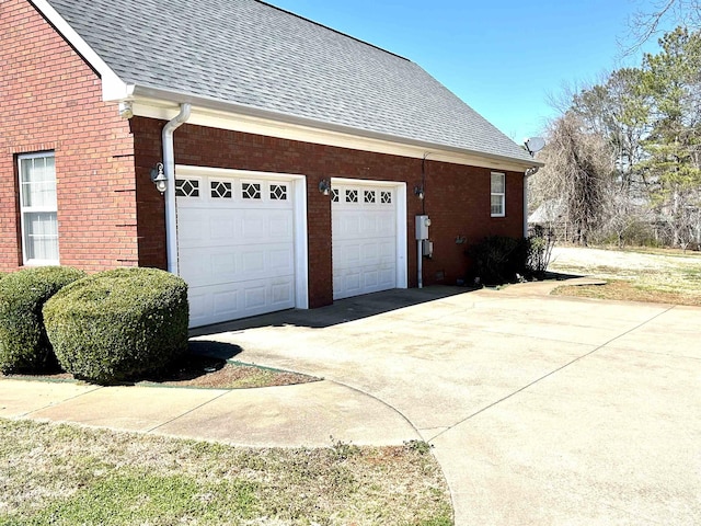 view of property exterior with a shingled roof, concrete driveway, and brick siding