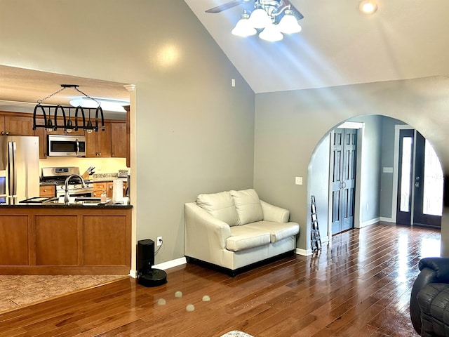 living area with high vaulted ceiling, arched walkways, baseboards, and hardwood / wood-style flooring