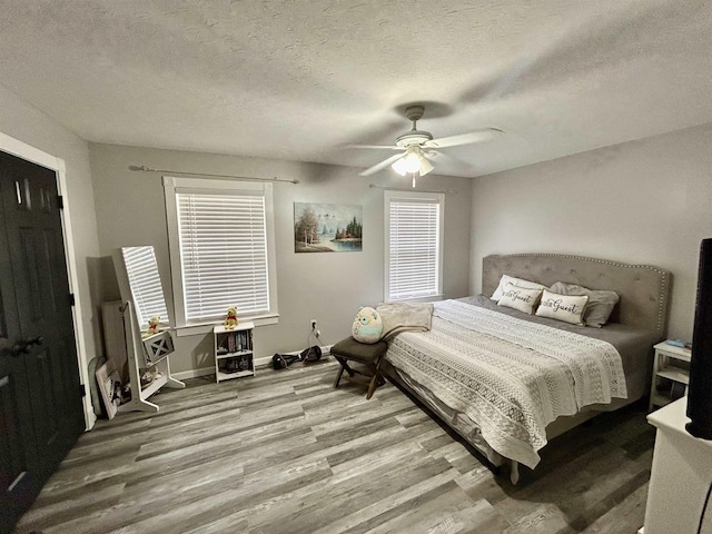 bedroom featuring ceiling fan, a textured ceiling, baseboards, and wood finished floors