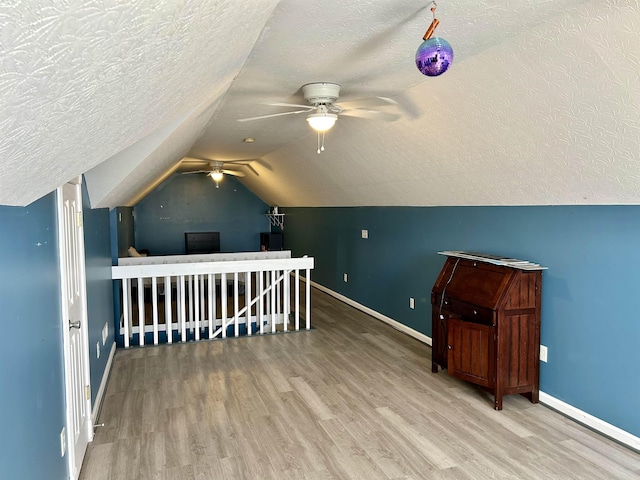 bonus room with a textured ceiling, baseboards, vaulted ceiling, and wood finished floors