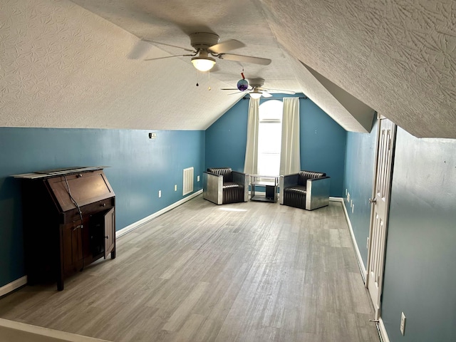 additional living space featuring a textured ceiling, wood finished floors, visible vents, baseboards, and vaulted ceiling