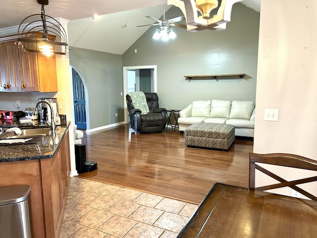 living area with lofted ceiling, arched walkways, ceiling fan with notable chandelier, baseboards, and light wood finished floors