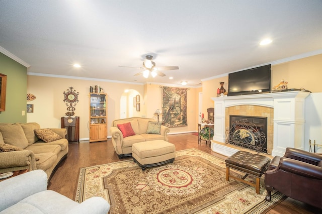 living room featuring ceiling fan, wood-type flooring, crown molding, and a tile fireplace