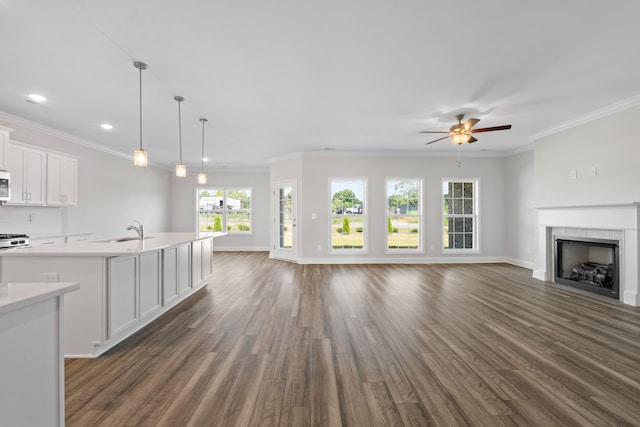 unfurnished living room featuring a tile fireplace, ceiling fan, sink, dark hardwood / wood-style floors, and ornamental molding