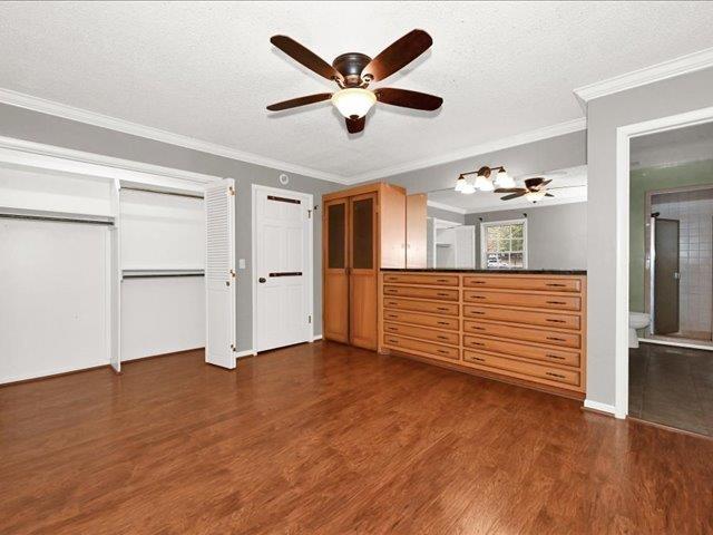 unfurnished bedroom with ensuite bathroom, ornamental molding, a textured ceiling, ceiling fan, and dark wood-type flooring