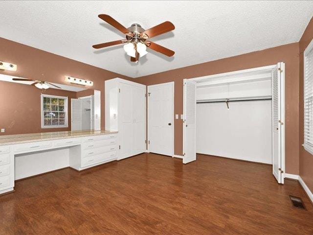 unfurnished bedroom featuring ceiling fan, built in desk, a textured ceiling, and dark wood-type flooring