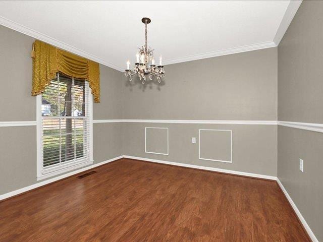 spare room with hardwood / wood-style flooring, ornamental molding, and a notable chandelier