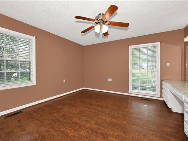 empty room with a textured ceiling, ceiling fan, built in desk, and dark hardwood / wood-style floors