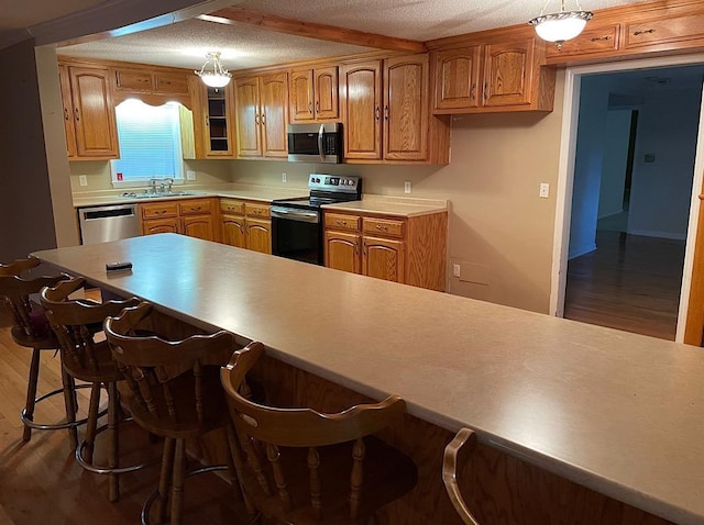 kitchen with light countertops, a breakfast bar area, stainless steel appliances, a sink, and wood finished floors