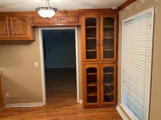 hall featuring light wood-style flooring, a textured ceiling, and baseboards
