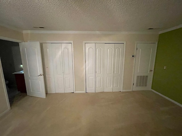 unfurnished bedroom with baseboards, two closets, crown molding, visible vents, and light colored carpet