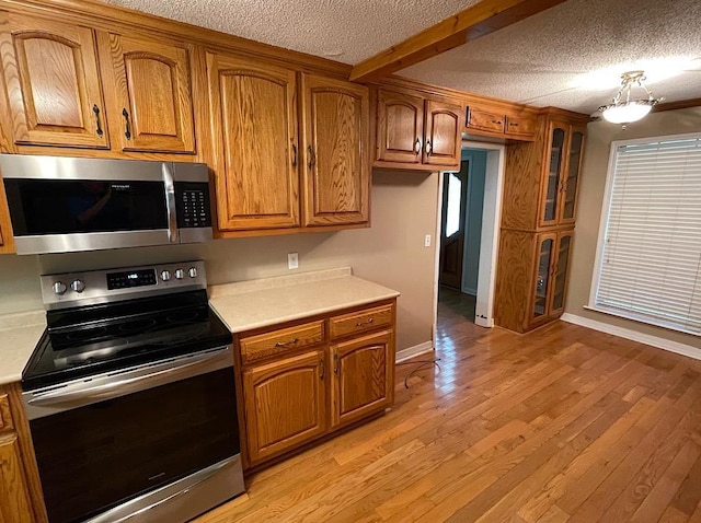 kitchen with light countertops, appliances with stainless steel finishes, a textured ceiling, brown cabinets, and light wood-style flooring