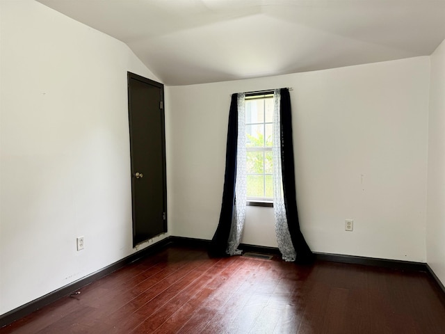spare room featuring baseboards, dark wood finished floors, and vaulted ceiling
